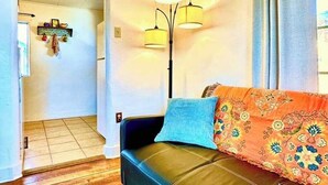 Una sala de estar con un sofá de cuero negro, un cojín estampado, una alfombra azul y una lámpara de pie.