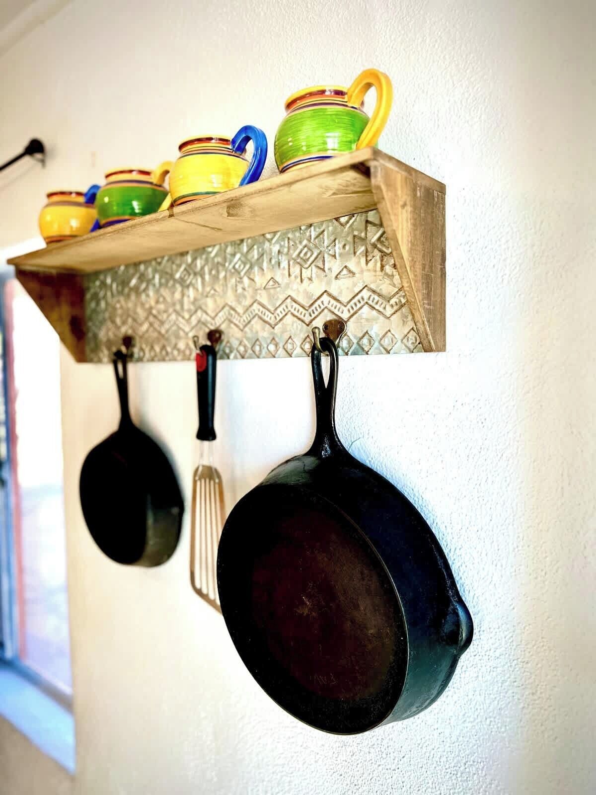 Une étagère en bois ornée de tasses en céramique aux couleurs vives et de casseroles noires suspendues.