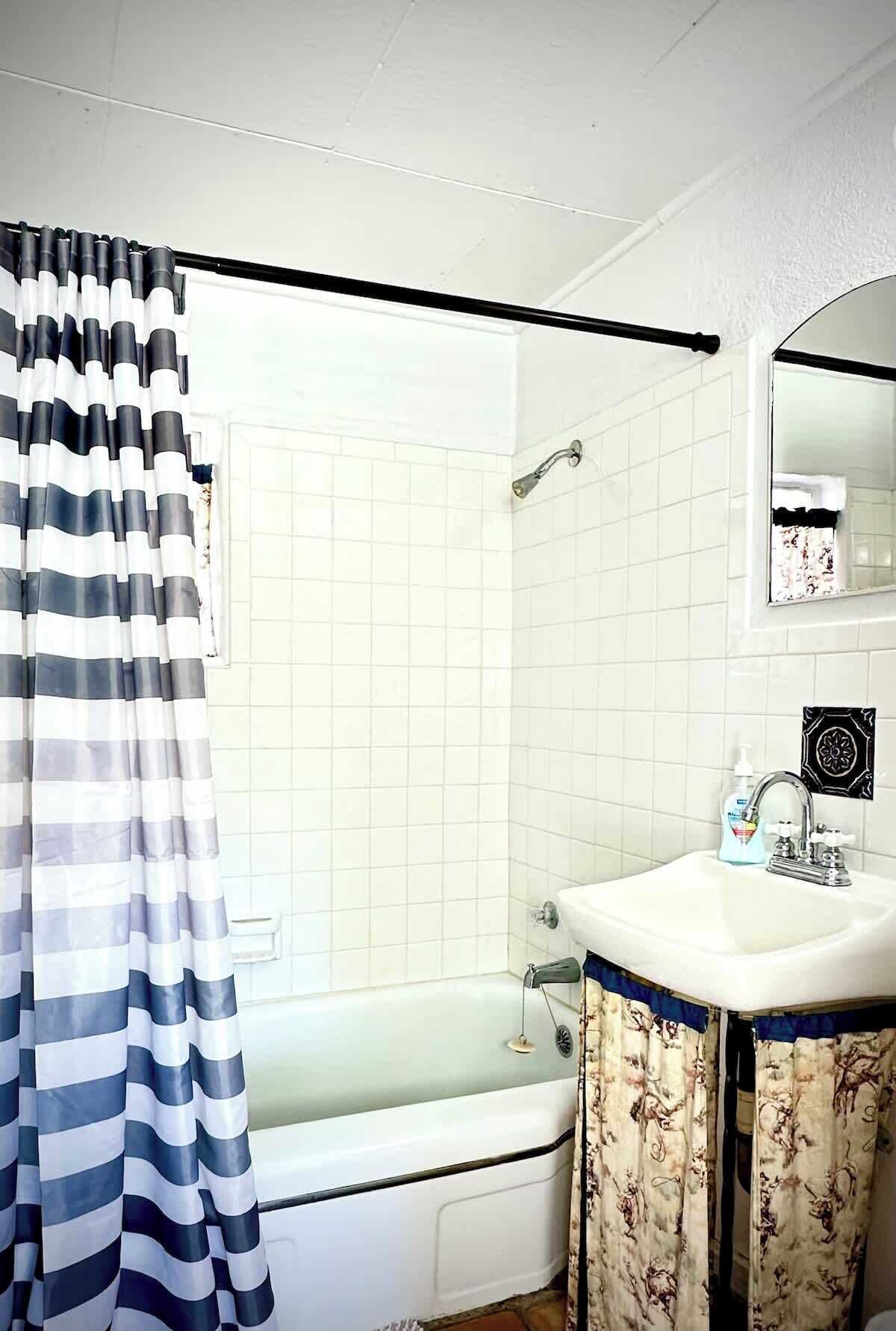 Une salle de bain avec une baignoire, une douche, un lavabo avec un miroir et un rideau à rayures.
