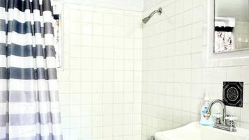 A bathroom with a bathtub, a shower, a sink with a mirror, and a striped curtain.