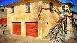 A two-story building with a red garage door, a staircase leading to the second floor, and a small balcony. - La Casita | Southwest Studio Near Downtown Raton (Raton)