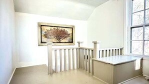 A room with a white wall, a framed painting, a wooden bench, and a window. - 1890s Carriage House \ Walk To Downtown (Raton)