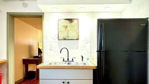 A compact kitchen with a black refrigerator, white cabinets, and a patterned rug on the wooden floor. - 1890s Carriage House \ Walk To Downtown (Raton)