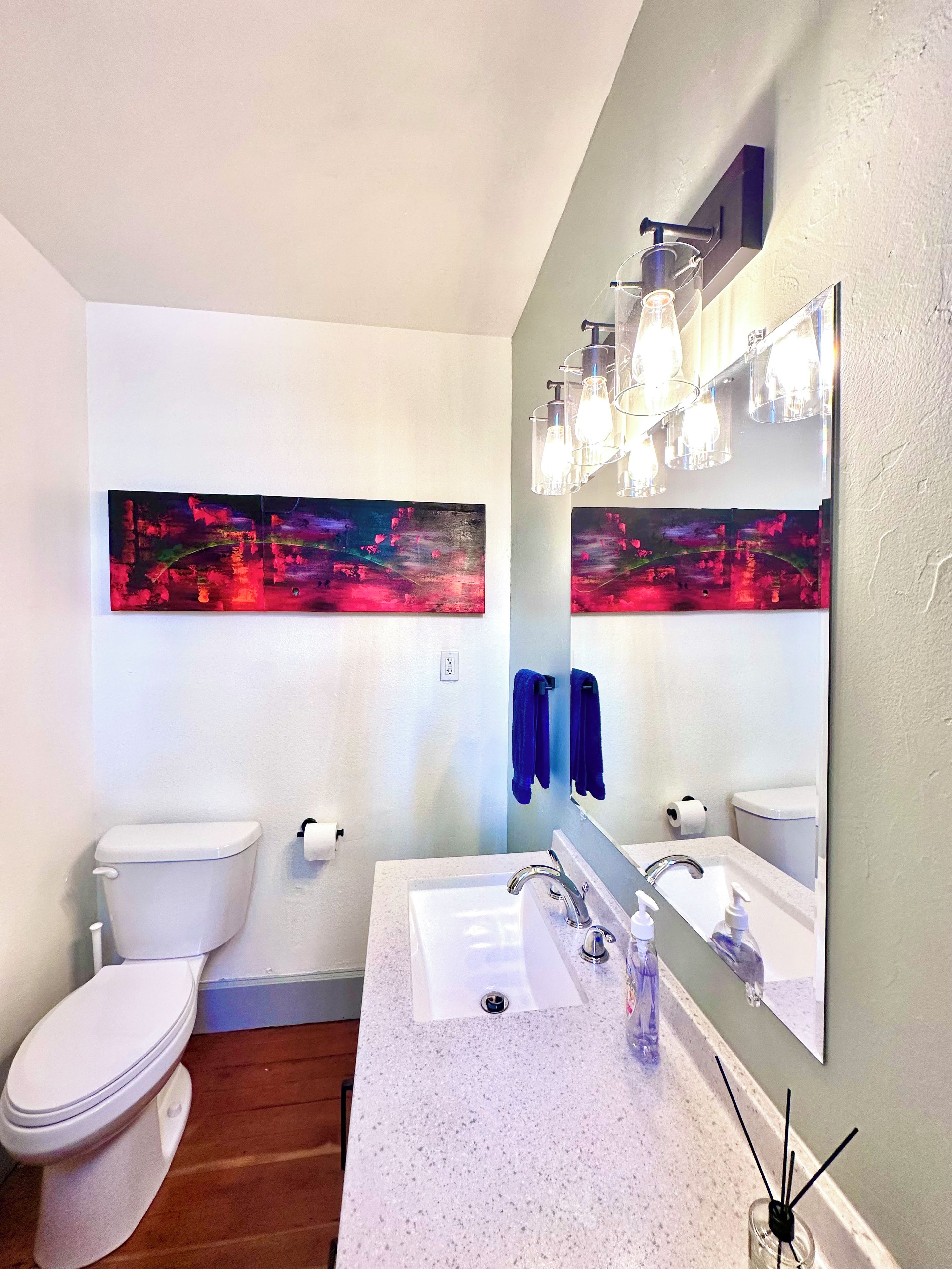 A bathroom with a white toilet, a sink with a mirror, and a wall-mounted light fixture.