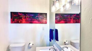 A bathroom with a white toilet, a sink with a mirror, and a wall-mounted light fixture.