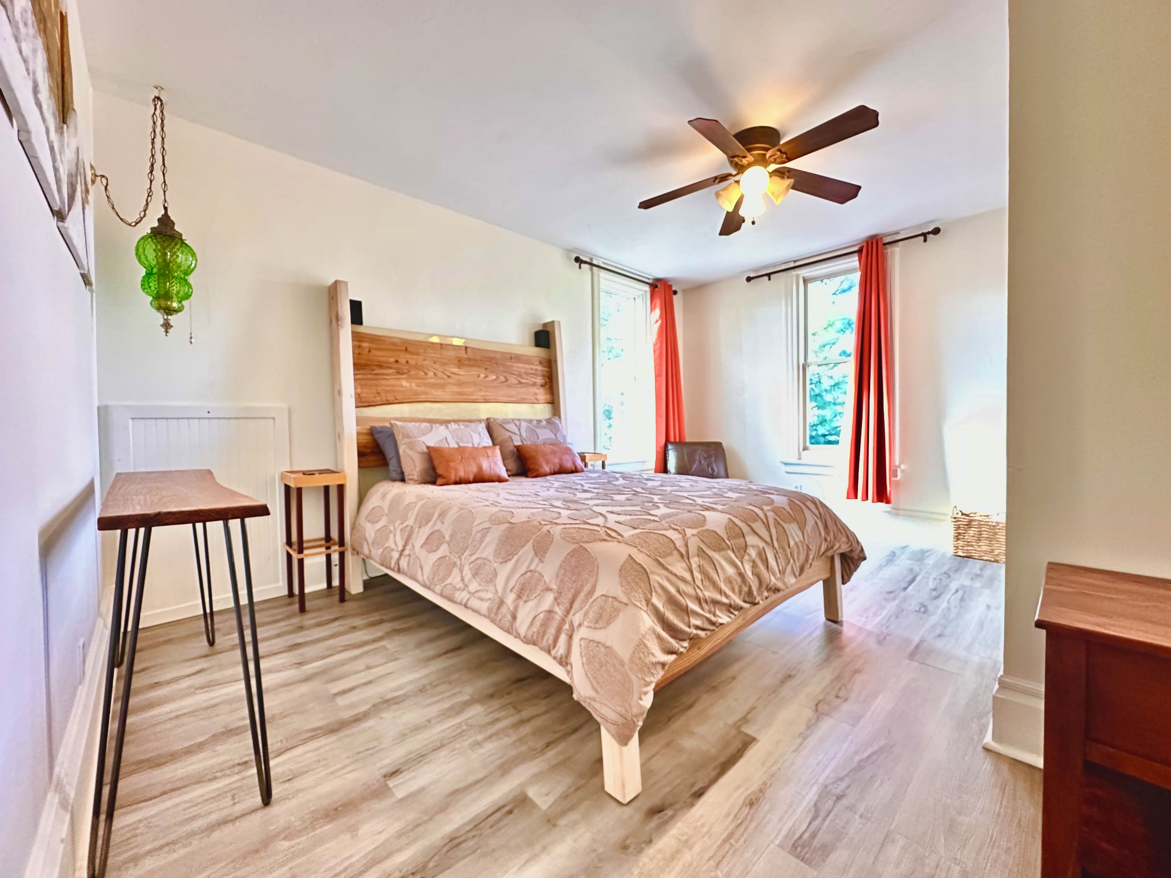 A bedroom with a wooden bed, a ceiling fan, a small table, and a chair.
