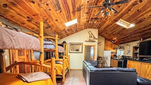A rustic cabin interior with a loft bed, a sofa, a dining table, and a kitchen area. - Capulin Volcano View House (Union County)