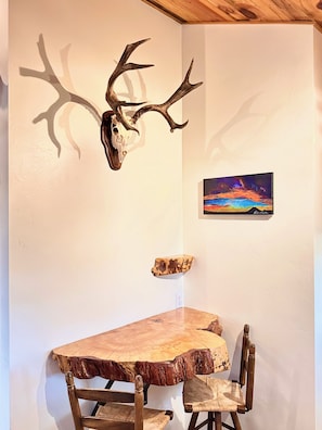 A dining area with a wooden table and chairs, a mounted deer skull, and a framed painting on the wall. - Capulin Volcano View House (Union County)