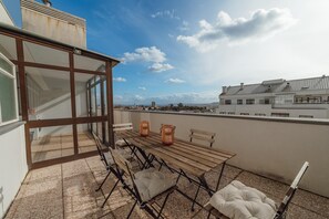 A rooftop terrace with a wooden table and chairs, two wicker baskets, and a view of the cityscape. - City Center Grand SEA View Terrace by Vacationy (Porto)