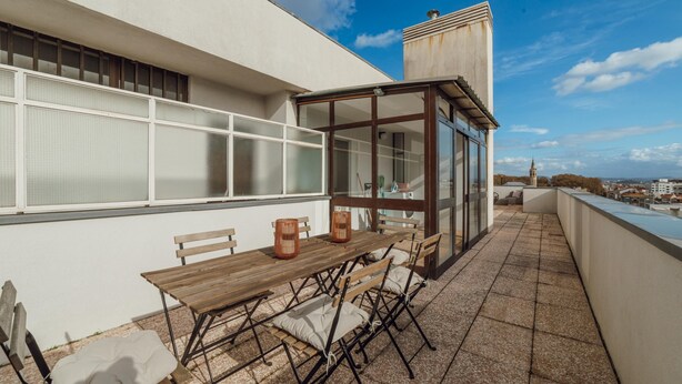 A rooftop terrace with a wooden table and chairs, a glass enclosure, and a city view. - City Center Grand SEA View Terrace by Vacationy (Porto)