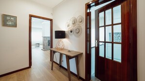 A hallway with a wooden floor, a table with a lamp, a decorative wall piece, and a door with glass panels. - City Center Grand SEA View Terrace by Vacationy (Porto)
