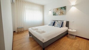 A modern bedroom with a large bed, a bedside table, a round side table, and a window with blinds. - City Center Grand SEA View Terrace by Vacationy (Porto)