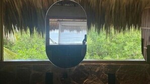 A room with a hanging chair, a window with a view of greenery, and a thatched roof. - Utopia Tiny Beach House

 (cozoaltepec tonameca)
