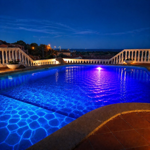 Una piscina de borde curvo, rodeada por una barandilla, con vista al mar de fondo.
