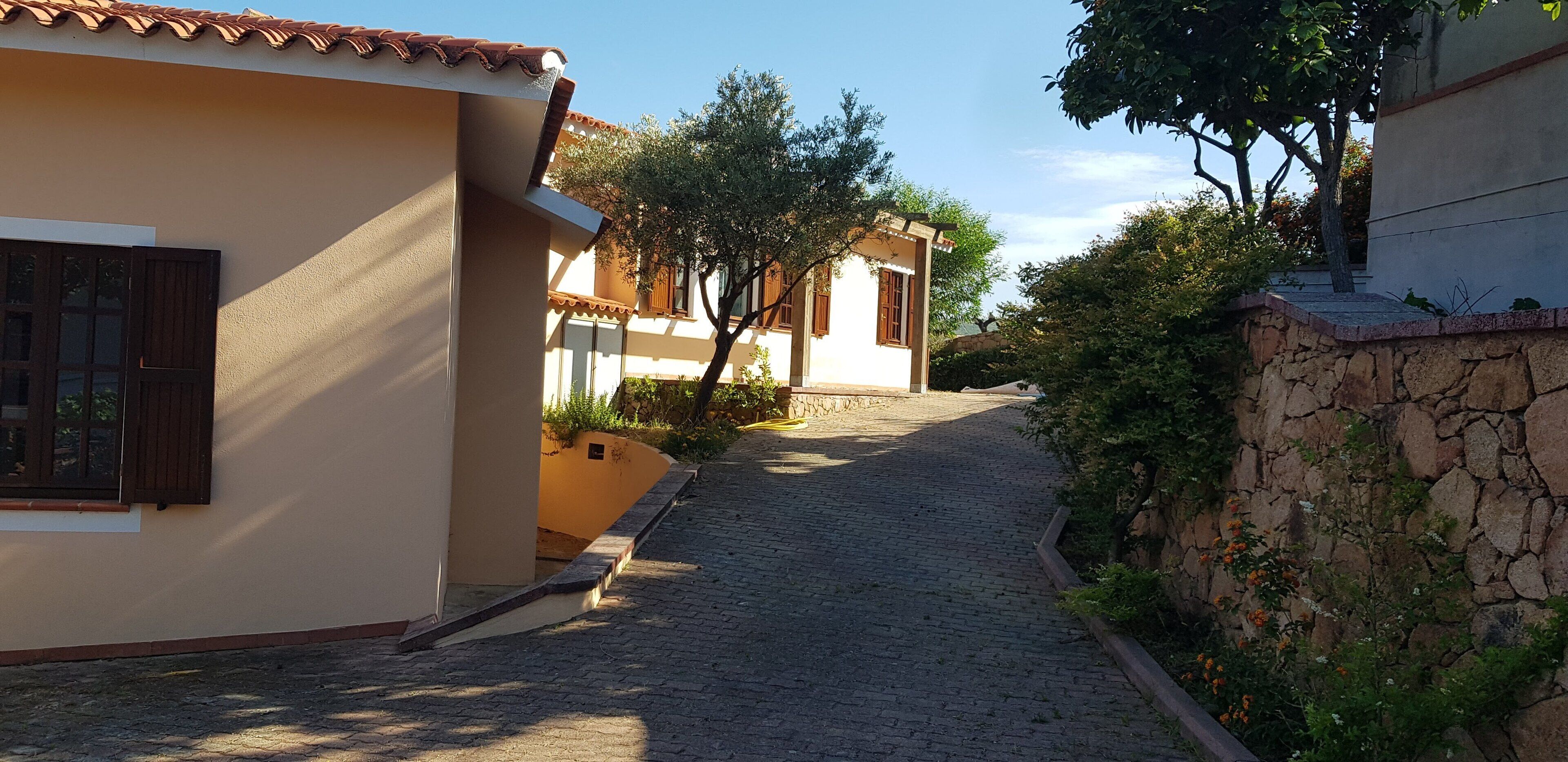 A narrow cobblestone street flanked by buildings with beige walls and brown shutters.