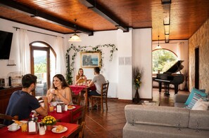 Comedor con mantel rojo, un piano y un sofá con cojines.