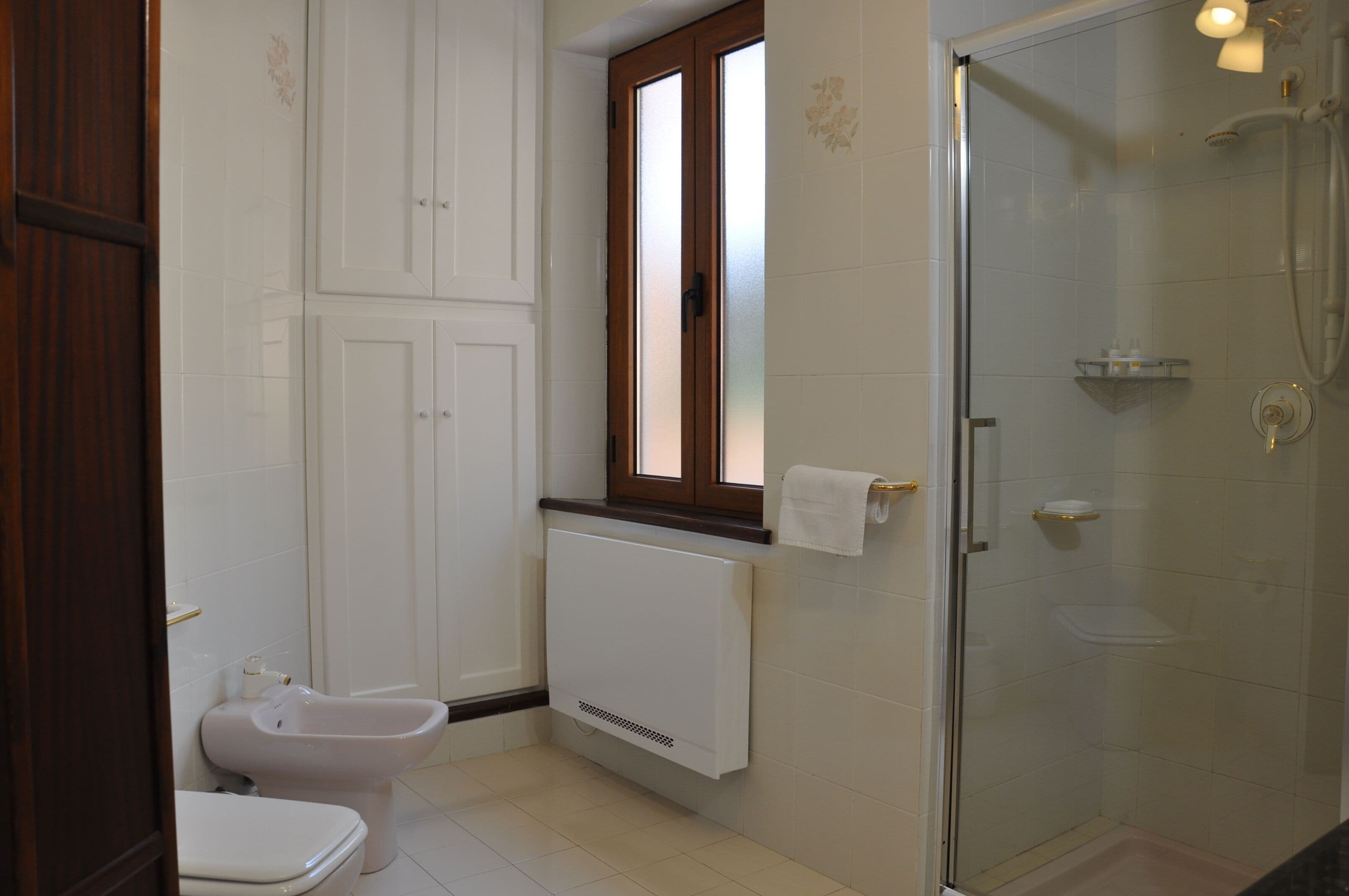 A bathroom with a toilet, bidet, shower, and a window.