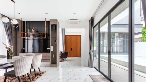 A modern interior with a dining area featuring a marble floor, a kitchen with a black countertop, and a large sliding glass door leading to a balcony. - Family-sized holiday house with private pool, perfect for families and friends! (Chonburi)
