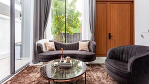 A modern living room with a curved sofa, a round coffee table, and a dark armchair. - Family-sized holiday house with private pool, perfect for families and friends! (Chonburi)