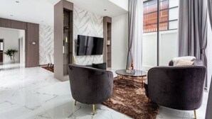A modern living room with a flat-screen TV, two black armchairs, a round coffee table, and a marble floor. - Family-sized holiday house with private pool, perfect for families and friends! (Chonburi)