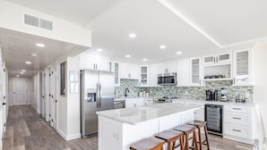 A modern kitchen with white cabinetry, a large island with stools, stainless steel appliances, and a tiled backsplash. - Beachfront-Luxury Renovated Condo For 13 w/Wrap Balcony @ Edgewater Beach Resort (Panama City Beach)
