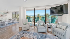 A modern living room with a dining area, a large TV, and a balcony with a view of the ocean. - Beachfront-Luxury Renovated Condo For 13 w/Wrap Balcony @ Edgewater Beach Resort (Panama City Beach)