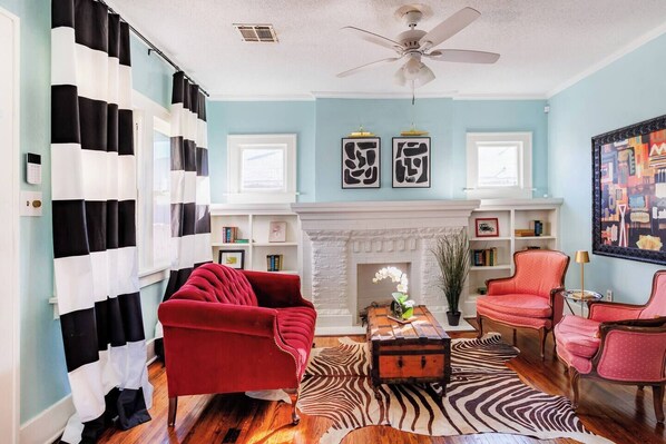 A living room with a fireplace, red armchairs, a zebra-patterned rug, and a ceiling fan.