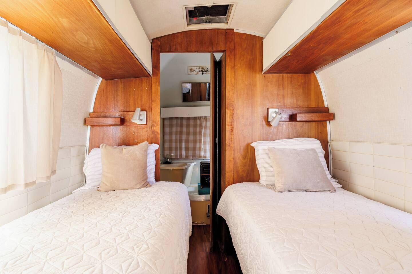 A compact RV interior with two beds, a kitchenette, and a small bathroom.
