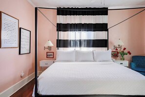 A bedroom with a bed, bedside tables, a lamp, a chair, and a wall with framed pictures.