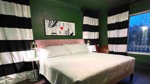 Een slaapkamer met een groot bed, gestreepte gordijnen, een schilderij aan de muur en een raam met uitzicht op gebouwen.