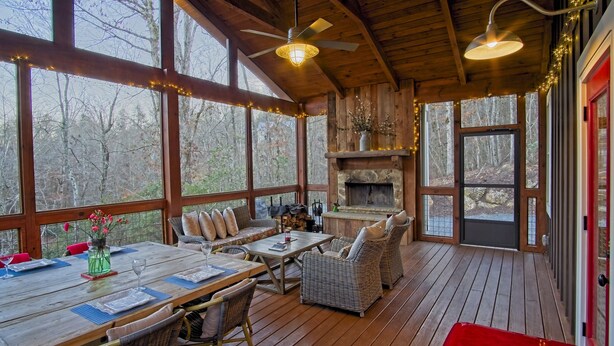 A wooden deck with a fireplace, wicker furniture, and a dining table set for four. - Vineyard Waterfall Cabin+Free Tasting  on Turkey Creek (Ellijay)
