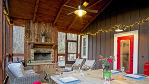 A cozy cabin interior with a stone fireplace, wicker furniture, and a dining table set for two. - Vineyard Waterfall Cabin+Free Tasting  on Turkey Creek (Ellijay)