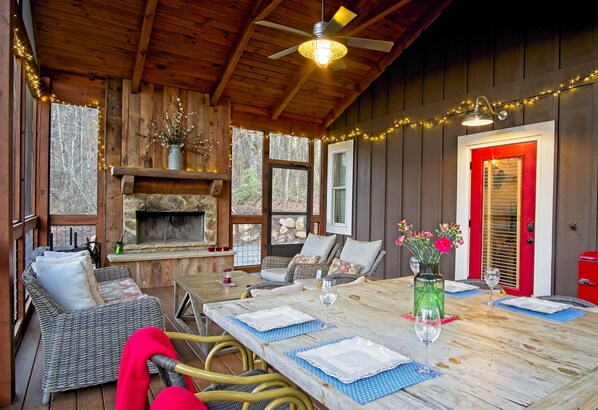 A cozy cabin interior with a stone fireplace, wicker furniture, and a dining table set for two. - Vineyard Waterfall Cabin+Free Tasting on Turkey Creek (Ellijay)
