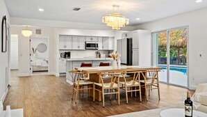 Een moderne keuken met witte kastjes, een eethoek met een houten tafel en stoelen, en uitzicht op een zwembad.