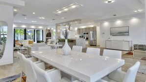 A modern, spacious living area with a large white dining table, white sofas, and a kitchen in the background. - Lynora's Luxe Estate Modern Design (Fort Lauderdale)