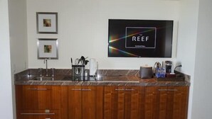 A kitchen with wooden cabinets, a granite countertop, a coffee machine, and a flat-screen TV mounted on the wall. - Gorgeous Studio The Reef Atlantis

 (Nassau)
