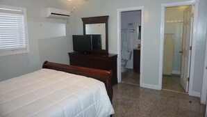Ein Schlafzimmer mit Bett, Kommode, Fernseher, Deckenventilator und Klimaanlage.