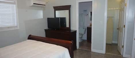 Une chambre à coucher comprenant un lit, une commode, un téléviseur, un ventilateur de plafond et un appareil de climatisation.