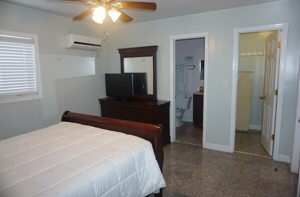 A bedroom with a bed, a dresser, a television, a ceiling fan, and an air conditioning unit.