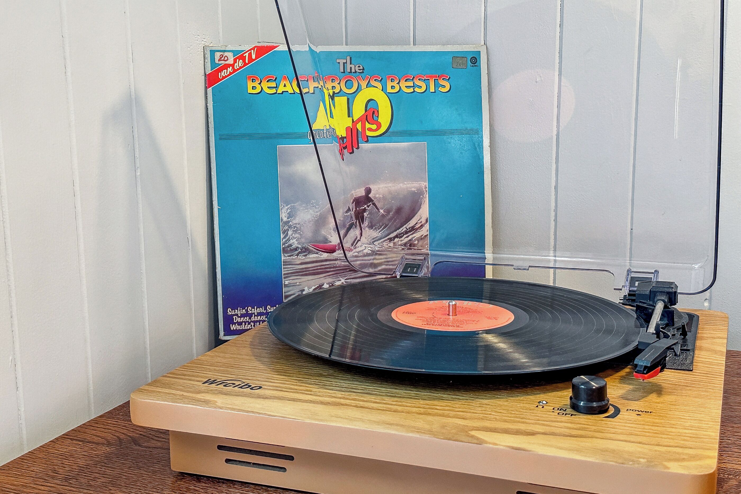 A turntable with a vinyl record and a book titled "The Beach Boys Best Hits" on a wooden table.