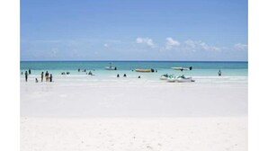 A beach with clear turquoise water, several boats, and people.