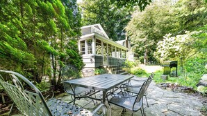 A patio with a table and chairs, surrounded by lush greenery and a house in the background. - Four Night Min! Lakeside Home With 800 Feet Of Association Beach! (Lakeside)