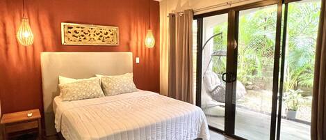 A bedroom with a bed, a ceiling fan, a nightstand, and a view of a garden through a sliding glass door.