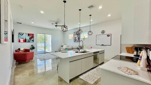 Una cucina moderna con isola centrale, illuminazione a sospensione e una poltrona rossa.