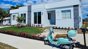 Una moderna casa a due piani con facciata bianca e dettagli in pietra, un vialetto lastricato e uno scooter parcheggiato.
