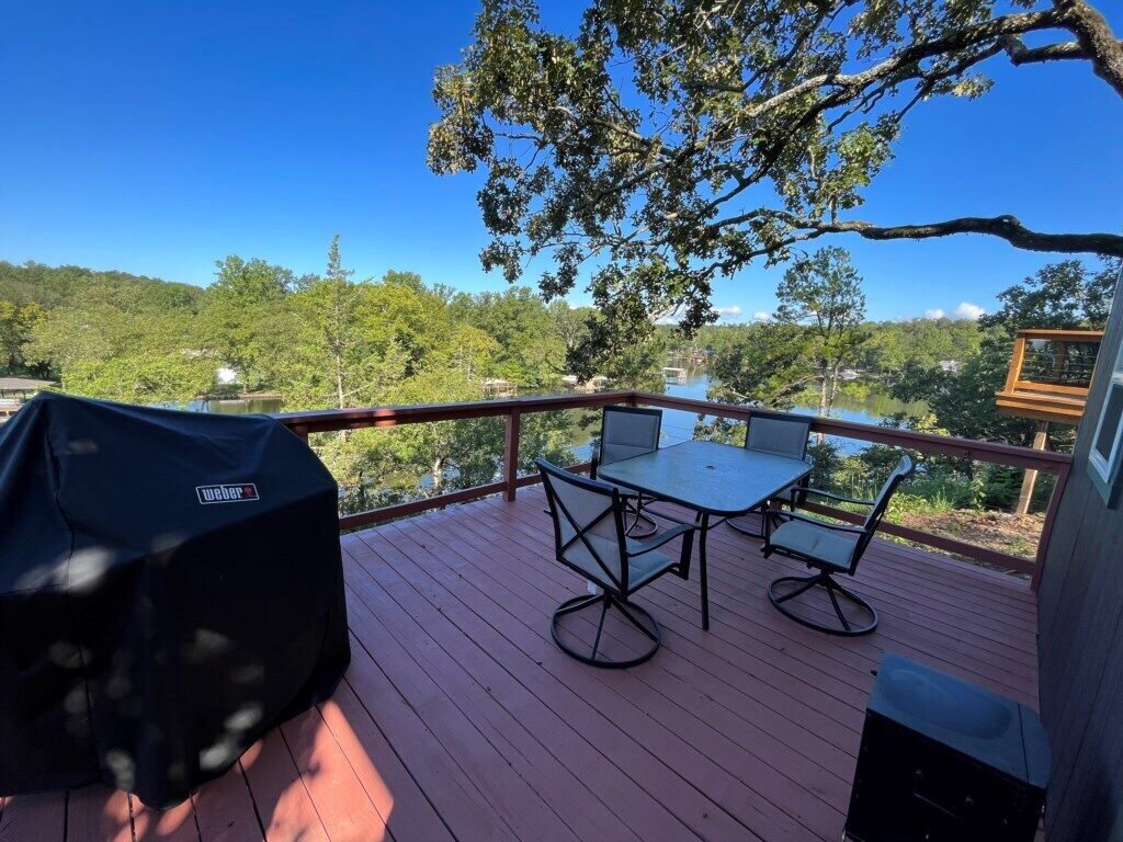 Terraza con mesa y sillas, con vista a un lago y zona boscosa.