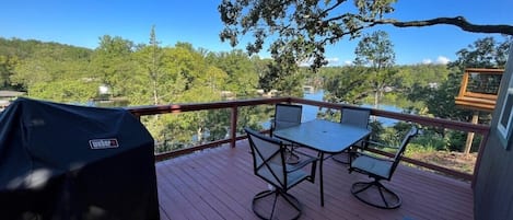 Terraza con mesa y sillas, con vista a un lago y zona boscosa.