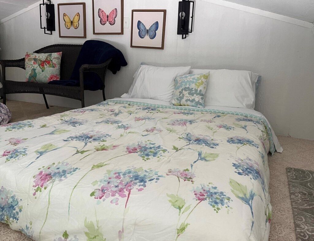 A bedroom with a floral bedspread, a wicker chair, and wall-mounted butterfly art.