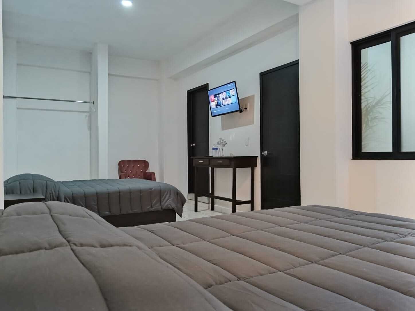 Quarto com duas camas, televisão na parede, escrivaninha e uma cadeira.