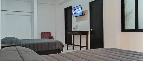 Quarto com duas camas, televisão na parede, escrivaninha e uma cadeira.
